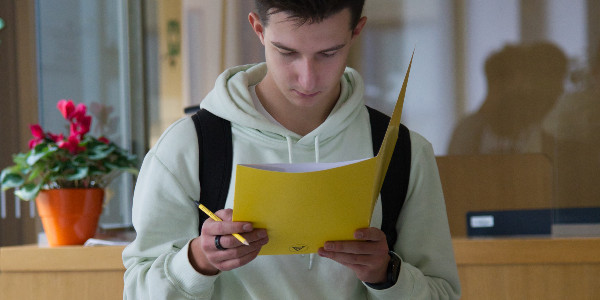 A highschooler is reading paper handouts while holding a pencil
